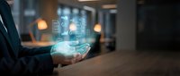 Businessman holding smartphone with glowing digital holographic interface displaying data analytics and technology concepts in modern office environment.