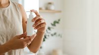 Woman applying hand sanitizer or moisturizing lotion from pump bottle for skincare, hygiene, and wellness routine at home.