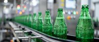 Green glass bottles with carbonated beverage moving on conveyor belt in industrial manufacturing facility production line.
