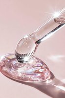 Clear cosmetic serum drop falling from dropper onto shimmering gel substance against pink background, with light reflections and sparkle effects.
