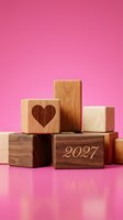 Wooden blocks arranged in staggered formation against vibrant pink background, featuring heart symbol and 2027 engraving, suitable for New Year campaigns and romantic designs.