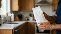 Man holding blank white box in modern kitchen, unboxing product or delivery package for advertising and marketing purposes.