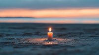Glowing candle on sandy beach at sunset creates peaceful atmosphere with orange sky reflection on water surface, spiritual meditation background.