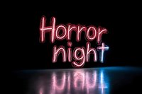 Glowing pink neon text saying Horror night reflected on dark surface with blue light accent, creating spooky atmospheric mood for Halloween or entertainment events.