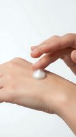 Caucasian hands applying white skincare cream or lotion on arm against neutral background for cosmetics and beauty product marketing.