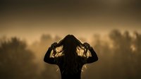 Silhouette of woman with long hair against golden sunset sky creating dramatic atmospheric mood for wellness and mindfulness concepts.
