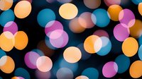Colorful defocused bokeh lights creating abstract background pattern with orange, purple and blue circular blurred spots on black backdrop.
