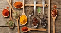 Colorful spices and herbs in wooden spoons on rustic table. Cooking ingredients including turmeric, paprika, cumin, bay leaves for culinary recipes.