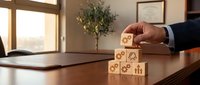 Businessman stacking wooden blocks with business icons on office desk, representing growth strategy, risk management, and corporate planning for success.
