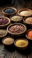 Assorted legumes and grains in wooden bowls on rustic wooden surface, including lentils, beans, and seeds for cooking and nutrition.