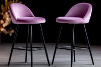 Modern pink velvet bar stools with curved backrest and black metal legs on dark background. Stylish contemporary furniture for kitchen counter or home bar.