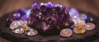 Amethyst crystal cluster surrounded by tumbled gemstones on dark slate, spiritual healing and meditation concept with warm bokeh background.