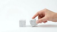 Hand placing white marble cube block next to another on clean surface for business strategy and building concepts.