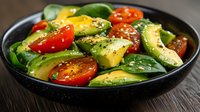 Fresh avocado slices with cherry tomatoes and baby spinach in black bowl, seasoned with herbs and spices, on wooden surface, healthy vegan salad.