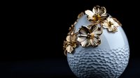 Elegant white ceramic egg with golden metallic flowers decoration on textured dimpled surface against dark background. Luxury Easter decor concept.