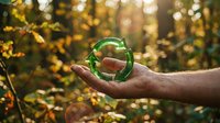 Male hand holding green recycling symbol in autumn forest with golden sunlight bokeh background representing environmental sustainability and eco-friendly lifestyle.