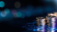 Stacked coins on digital market data with blue bokeh background reflecting financial growth and investment concept in dramatic lighting.