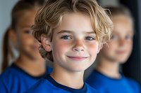 Young caucasian boy with curly blonde hair, freckles and bright smile wearing blue t-shirt, with diverse group of children in background, soft focus portrait.