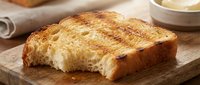 Toasted bread slice with golden-brown crust on wooden cutting board, fresh baked goods for breakfast, bakery, and culinary content.
