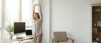 Young businesswoman stretching arms above head during work break in modern office with natural light for wellness and productivity.