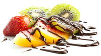 Fresh fruit slices of strawberry, mango and kiwi drizzled with dark chocolate sauce on white background, isolated food composition for dessert menu.