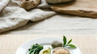 Freshly prepared ingredients including green vegetables, pasta, mushrooms and grains arranged on white plate with linen cloth and wooden utensils for cooking preparation.