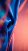 Abstract flowing fabric with vibrant blue and coral pink gradient colors, soft folds and curves creating dynamic movement, suitable for modern design backgrounds.