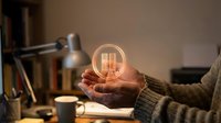 Hands holding glowing light bulb with books symbolizing creative ideas, innovation and knowledge in cozy study environment for educational content.