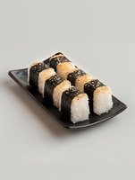 Fresh sushi rolls with nori seaweed and white rice topped with sesame seeds served on black rectangular ceramic plate against neutral background.