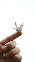 Close-up of hand holding delicate paper origami crane on fingertip against white background, symbolizing peace, hope, and mindfulness for wellness and meditation concepts.