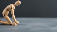 Wooden mannequin figure in defeated posture sitting on floor against dark background expressing depression, failure, and emotional distress concepts.
