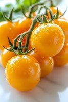 Fresh yellow cherry tomatoes on vine with water drops, macro shot showing vibrant color and natural texture against white marble background.