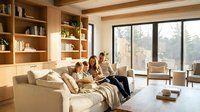 Family relaxing together on comfortable sofa in modern living room with built-in bookshelves and large windows creating cozy home atmosphere.