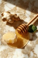 Fresh ginger root with honey dipper, golden honey and mint leaf on marble surface in warm sunlight, natural wellness and healthy food concept.