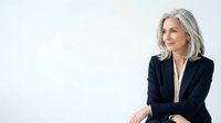 Mature woman with gray hair wearing dark blazer against white background, professional portrait for business and corporate use.