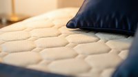 Comfortable mattress with quilted surface and dark navy pillow resting on top, showcasing bedding comfort and sleep quality for home decor and wellness content.