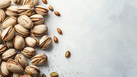 Fresh roasted pistachios scattered on light gray concrete background with copy space, top view. Natural healthy snack food photography.