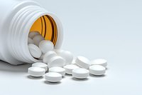 White prescription pills spilling from orange pharmacy bottle on light background, medical concept for healthcare and pharmaceutical industry.
