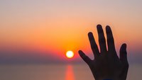 Silhouette of human hand reaching toward golden sunset over calm water creating peaceful moment of connection with nature and tranquil evening atmosphere.
