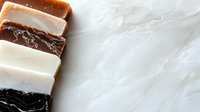 Handmade soap bars arranged in gradient color palette from black to white on marble background, showing natural organic texture and artisanal craftsmanship.