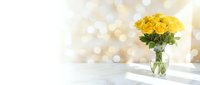 Fresh yellow roses in glass vase on white marble table with golden bokeh lights background for home decor and romantic occasions.