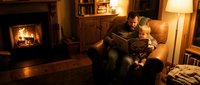 Father and young son reading book together on couch by warm fireplace in cozy living room creating bonding moment for family lifestyle content.