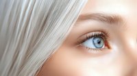 Close up view of bright blue eye with long eyelashes and platinum blonde hair, showing natural beauty and pure skin texture on soft beige background.
