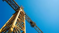 Construction crane tower against clear blue sky viewed from below showing industrial steel framework and mechanical engineering structure.