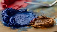 Artist palette with mixed blue and brown oil paints on wooden surface with paintbrush and canvas in background for creative artwork and painting projects.
