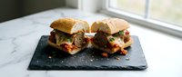 Gourmet meatball sliders with melted cheese and red sauce on toasted buns, served on a black slate board near a bright window for restaurant or food blog use.