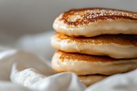 Fluffy stacked pancakes with golden-brown cinnamon sugar topping on white cloth. Breakfast food photography for culinary and recipe content.