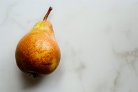 Fresh ripe pear with rustic speckled skin on white marble background, minimalist food photography perfect for healthy eating blogs and culinary content.