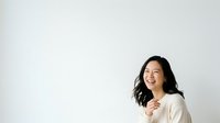 Young East Asian woman with long black hair smiling while wearing a cream-colored sweater against a white background, suitable for lifestyle, wellness, and corporate marketing materials.
