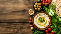 Middle Eastern appetizer spread with hummus, fresh vegetables, olives, chickpeas and flatbread on rustic wooden background with copy space. Top view.